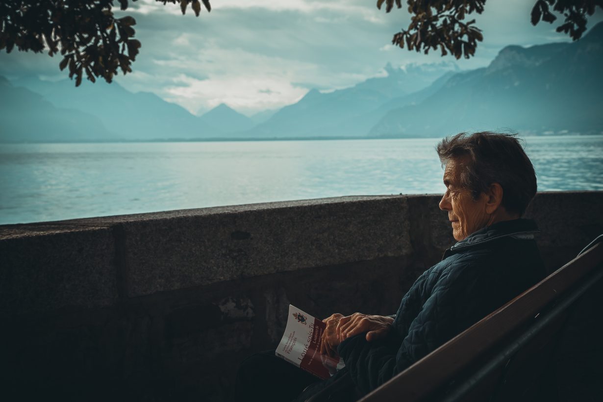 old man sitting on a bench overlooking a body of water