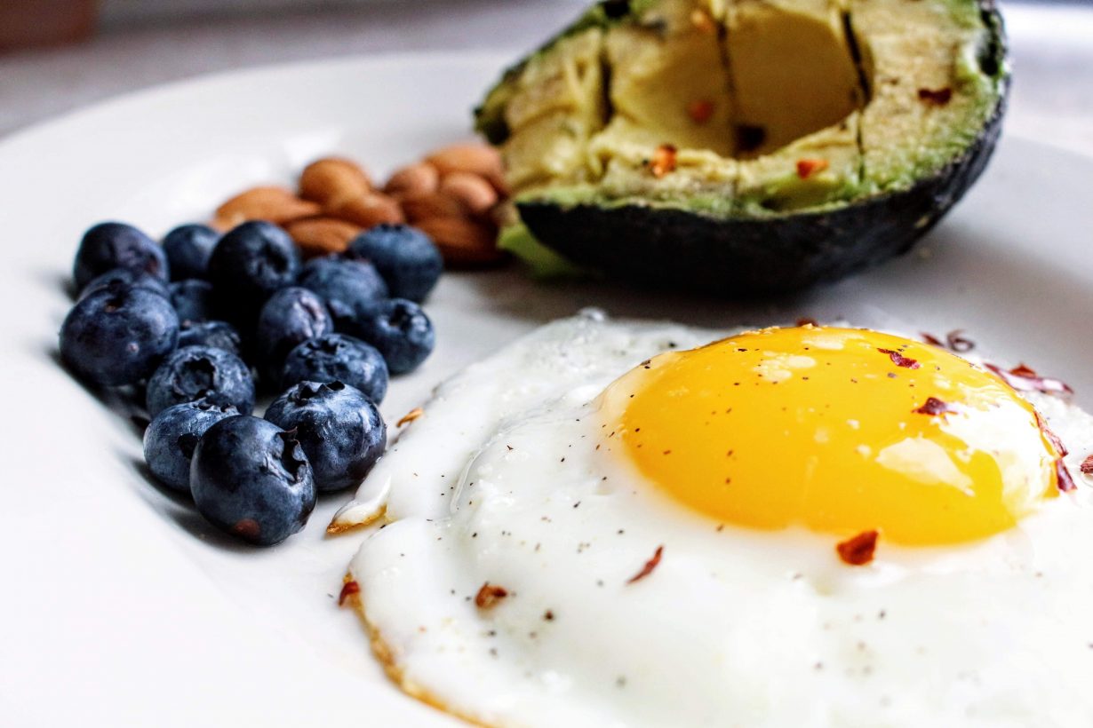fried egg with blueberries and avocado and nuts on a white plate