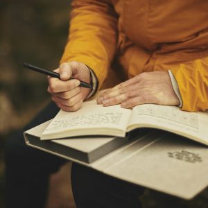 person holding a journal, pen and a book in their lap