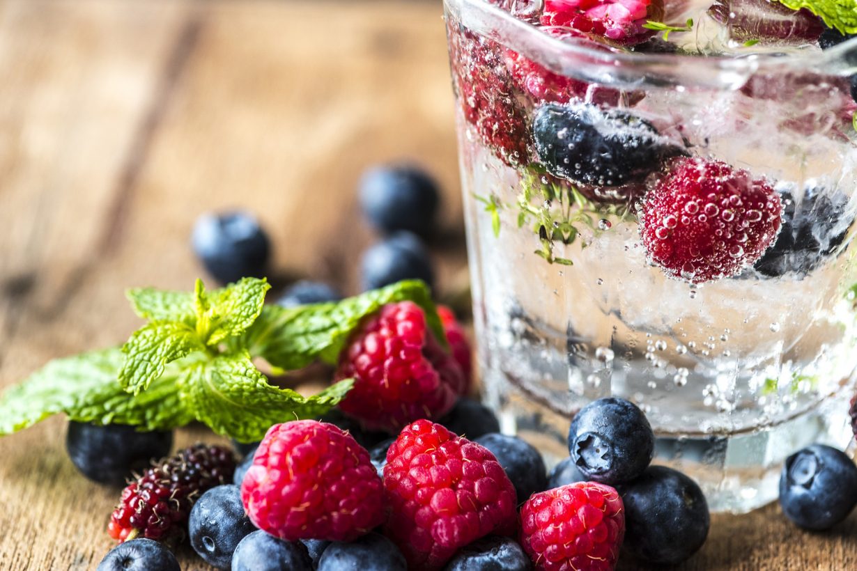 sparkling clear drink in a glass with floating berries inside