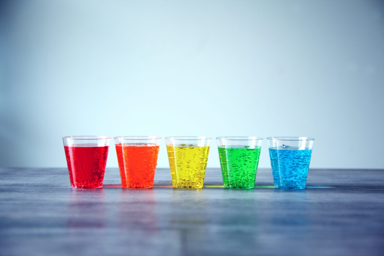 5 glasses lined up with rainbow colored fizzy drinks