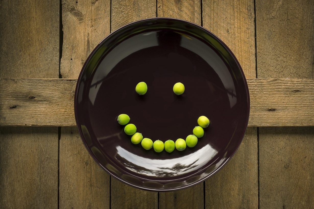black plate with a smiley face made of peas