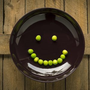 black plate with a smiley face made of peas