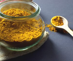 clear glass jar filled with turmeric and a wooden spoon next to it