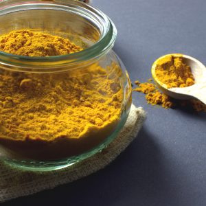 clear glass jar filled with turmeric and a wooden spoon next to it