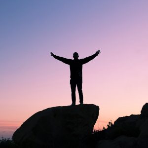 person silhouetted against the sky with arms raised up