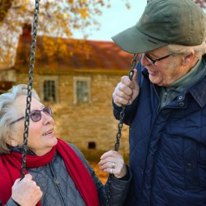 an old woman on a swing looking at an old man in a hat