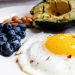 friend egg, blueberries, almonds and and avocado on a white plate