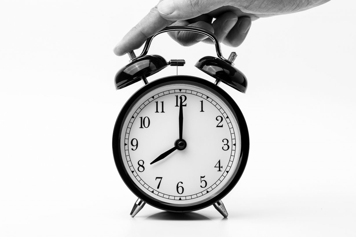 black and white photo of hand pushing a bell alarm clock