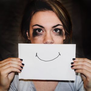 woman who looks like she's been crying holding a smiling face picture in front of her mouth