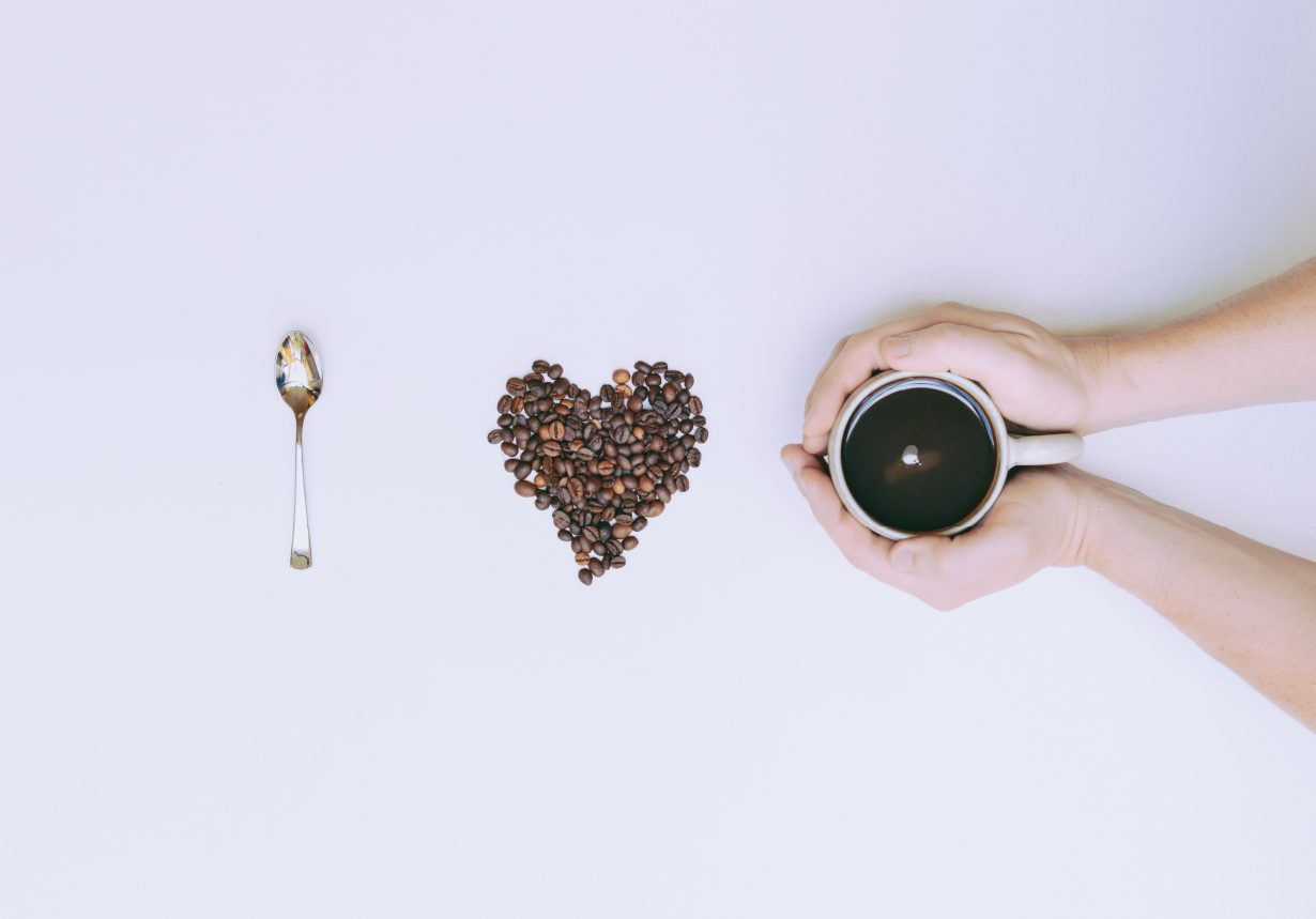 I love coffee spelled using a spoon, a heart made of coffee beans and a person holding a cup of coffee