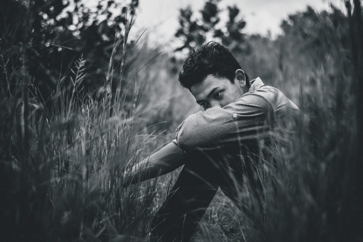 photo in black and white of a young man sitting in high grass looking sad