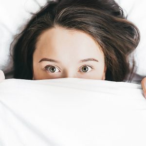 woman laying in a bed with sheets up over her face