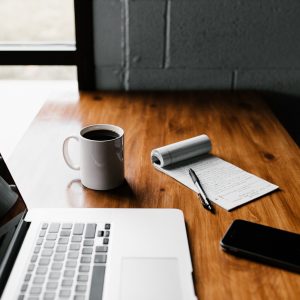 desk with a lap top, cup of coffee and a note pad