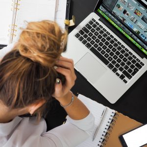 woman anxiously holding her head sitting in front of a laptop