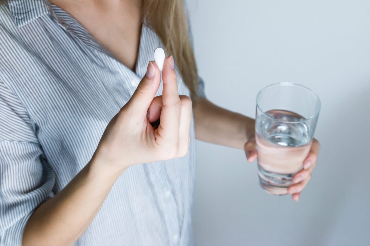 woman holding a white pill and a glass of water