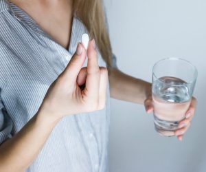 woman holding a white pill and a glass of water