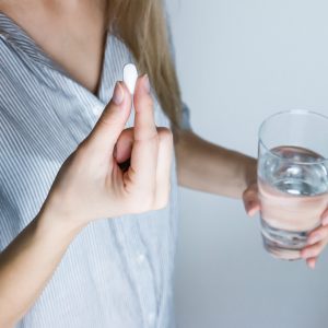 woman holding a white pill and a glass of water