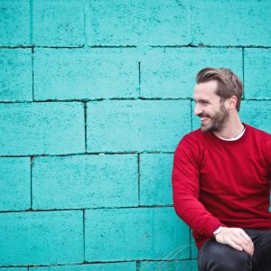 man in red shirt leaning against a teal wall