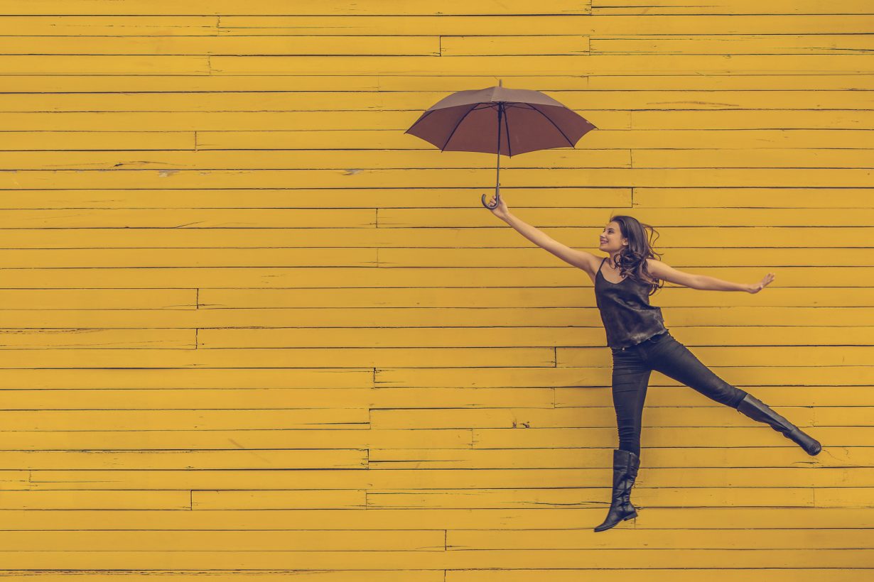 woman floating against a yellow wall with an umbrella
