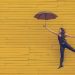 woman floating against a yellow wall with an umbrella
