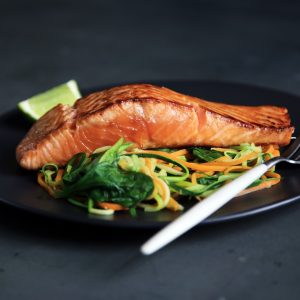 salmon fillet on a bed of vegetables on a black plate