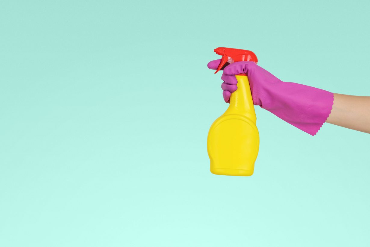 person wearing a pink rubber glove spraying a yellow spray bottle