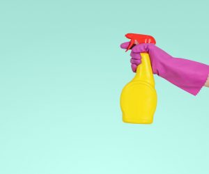 person wearing a pink rubber glove spraying a yellow spray bottle