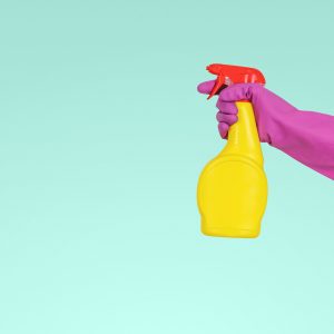 person wearing a pink rubber glove spraying a yellow spray bottle