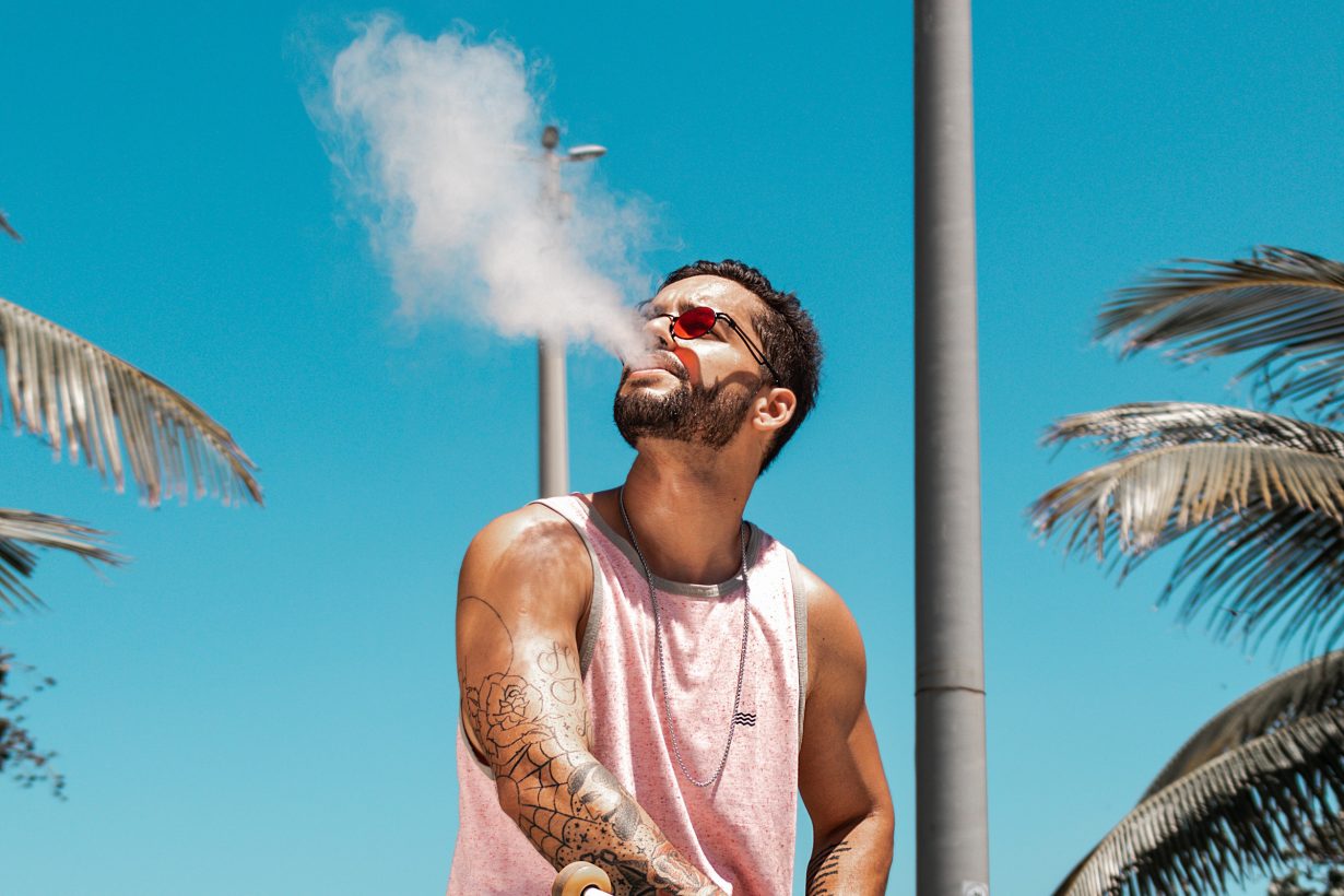 man sitting in sunshine blowing out smoke from his mouth