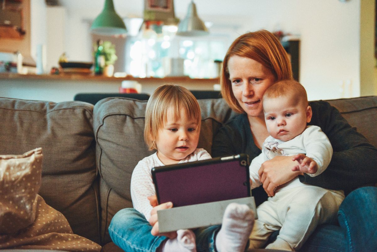 woman sitting with her two kids looking at a tablet