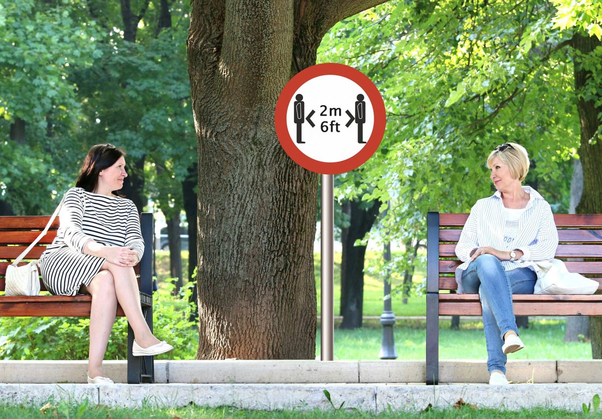 two women sitting 6 feet apart on park benches