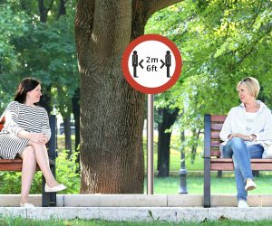 two women sitting 6 feet apart on park benches