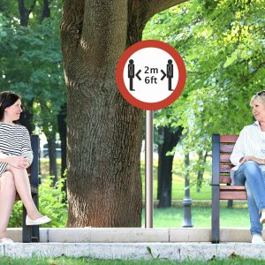 two women sitting 6 feet apart on park benches