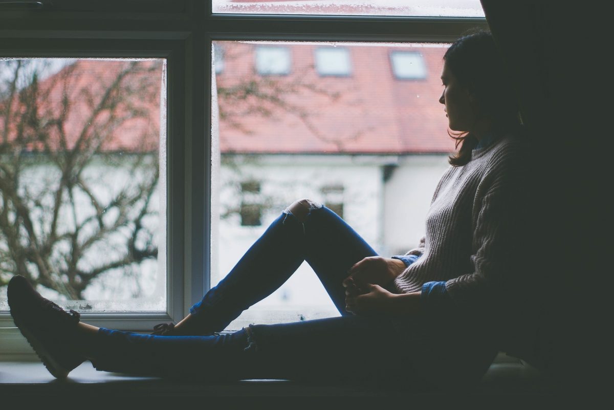 woman sitting on a window sill looking out her window