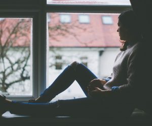 woman sitting on a window sill looking out her window