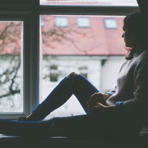 woman sitting on a window sill looking out her window