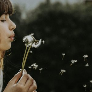 woman blowing on a dandelion