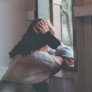 woman sitting in front of a window looking lonely