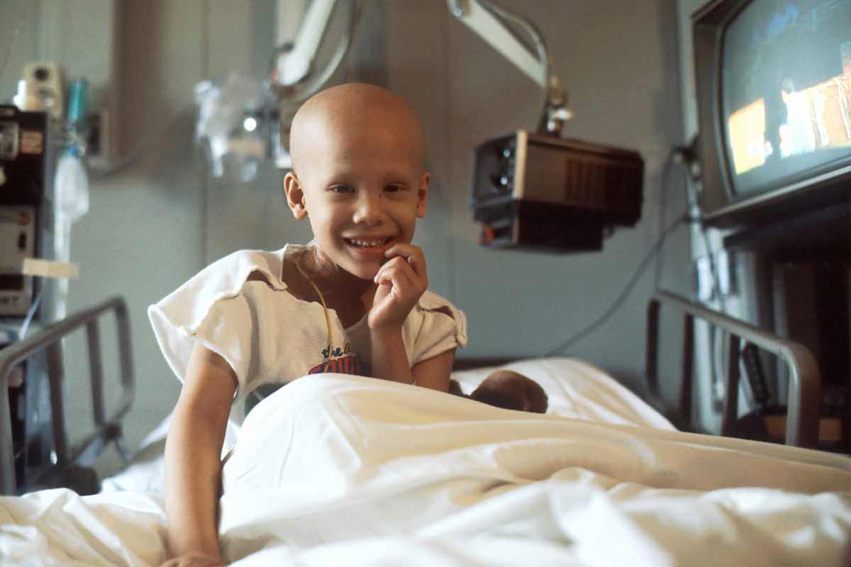 little child smiling in a hospital bed with a bald head