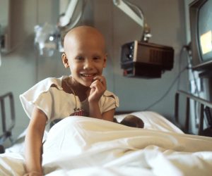 little child smiling in a hospital bed with a bald head