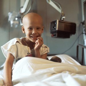 little child smiling in a hospital bed with a bald head