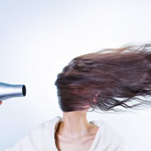 person blow drying their hair in front of their face