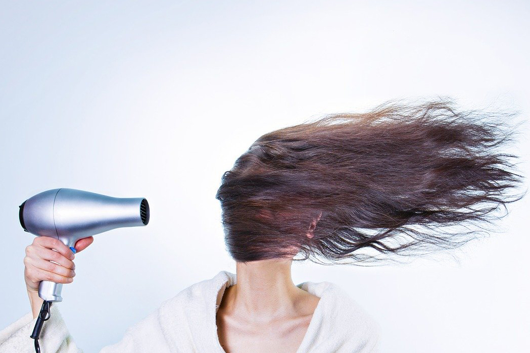 person blow drying their hair in front of their face