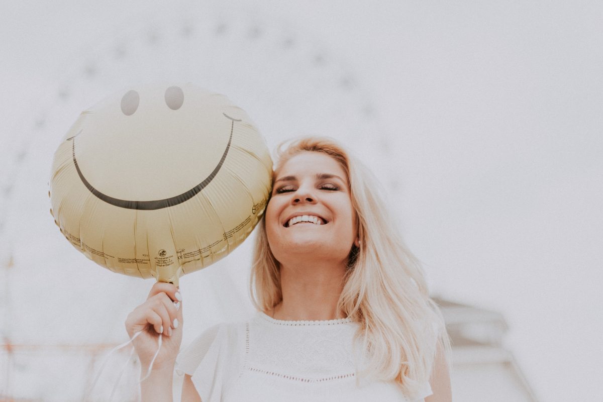 woman smiling while holding a smiley balloon