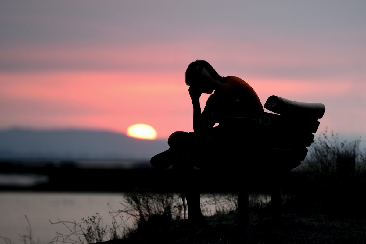 silhouette of a person sitting on a bench holding their head
