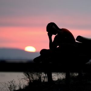 silhouette of a person sitting on a bench holding their head