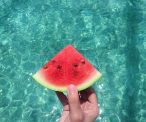 person holding a watermelon slice above aqua colored water