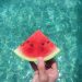 person holding a watermelon slice above aqua colored water