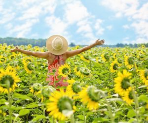 woman standing with outstretched arms in a sunflower field